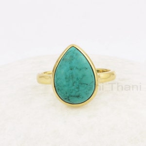 Könnte beinhalten: Ein goldener Ring mit einem türkisfarbenen tropfenförmigen Stein.