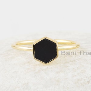 Può includere: Un anello d'oro con una pietra esagonale nera. L'anello è su uno sfondo bianco.  Bani Thani.