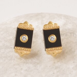 May include: A pair of gold earrings with black rectangular stones and a small clear rhinestone in the center of each stone.