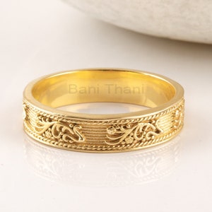 Może przedstawiać: Złoty pierścionek z ozdobnym wzorem kwiatowym. Wewnątrz obrączki widoczny jest napis "Bani Thani".
