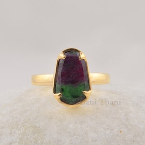 Puede incluir: Un anillo de oro con una piedra preciosa verde y roja. La piedra preciosa está engastada en un engaste de bisel y tiene un corte facetado.