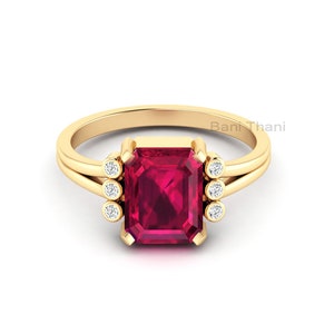 May include: A gold ring with a large, square-shaped ruby gemstone surrounded by smaller diamonds. The ring has a split shank design.