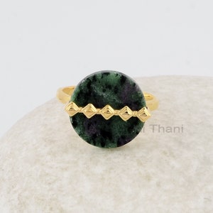 Peut inclure: Une bague en or avec une pierre précieuse verte sertie dans un bézel rond. La bague a une bande d'or avec une rangée de petits diamants en or.