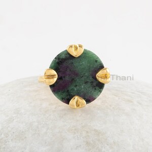 Könnte beinhalten: Ein Ring mit einem grünen und violetten Edelstein und goldenen Akzenten. Der Ring hat einen runden Stein, der in eine goldene Fassung mit vier goldenen Akzenten gefasst ist.