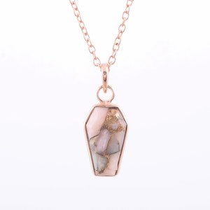 K&ouml;nnte beinhalten: Eine Halskette aus ros&eacute;goldener Kette mit einem ros&eacute;goldenen und goldenen Anh&auml;nger in Sargform. Der Anh&auml;nger ist aus einem ros&eacute;goldenen und goldenen Stein gefertigt.