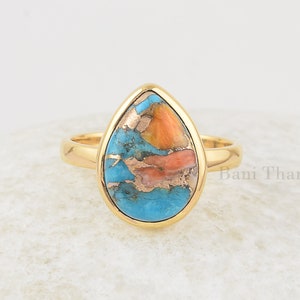 Könnte beinhalten: Ein goldener Ring mit einem tropfenförmigen Türkis-Stein. Der Stein hat eine Mischung aus blauen, orangen und braunen Farben.