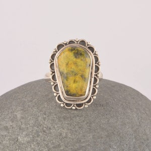 May include: A silver ring with a yellow and green gemstone set in a decorative, scalloped bezel.