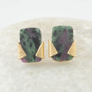 May include: A pair of gold earrings with green and pink gemstone rectangular stones. The stones have a mottled pattern and are set in gold with a triangular design on each side.