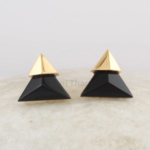 May include: A pair of black and gold triangle shaped earrings. The earrings are made of a black material with a gold top.