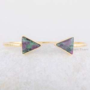 Può includere: Bracciale rigido in oro con due accenti di pietra preziosa triangolari verdi e rosa. Il bracciale è aperto e regolabile.