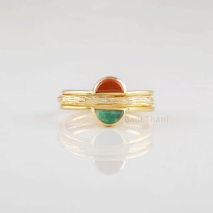 Op de afbeelding: Drie gouden ringen met een getextureerde band. De bovenste ring heeft een rode steen, de middelste ring heeft een getextureerde band en de onderste ring heeft een groene steen.