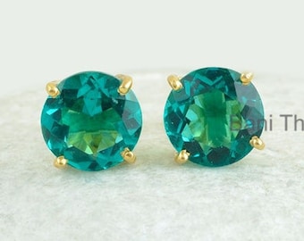 Puede incluir: Un par de pendientes de botón de oro con piedras preciosas redondas de color verde. Los pendientes están sobre un fondo blanco.