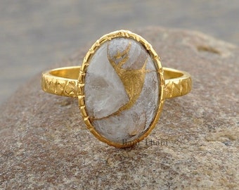 May include: Gold ring with an oval-shaped white stone with gold flecks. The ring has a textured band.