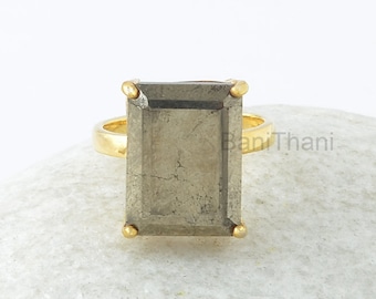 Puede incluir: Un anillo de oro con una piedra rectangular grande de color gris. La piedra tiene un acabado texturizado y metálico.