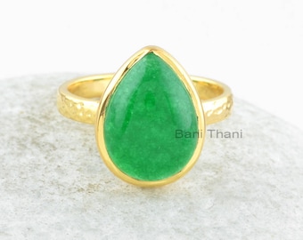 Pode incluir: Um anel de ouro com uma gema verde em forma de lágrima. O anel tem uma banda texturizada.