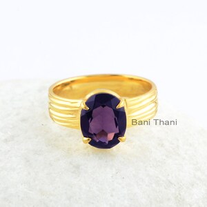 May include: A gold ring with a deep purple oval gemstone. The ring has a textured band with multiple ridges.