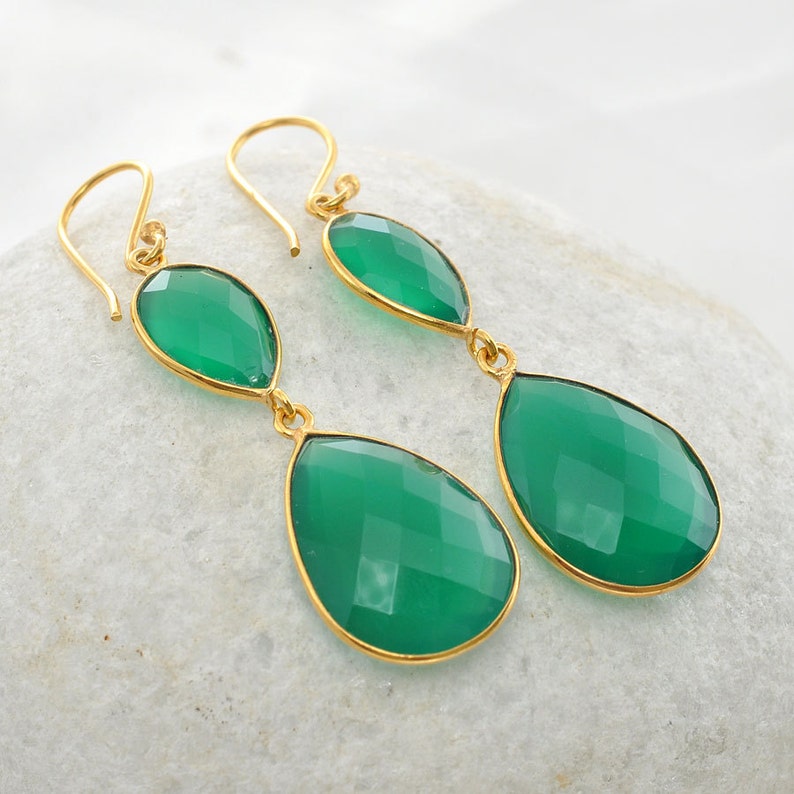 Op de afbeelding: Een paar gouden oorbellen met twee groene edelstenen in druppelvorm. De oorbellen zijn gemaakt van goud en hebben een eenvoudig ontwerp.