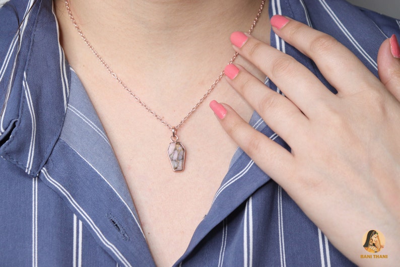 K&ouml;nnte beinhalten: Eine Halskette aus ros&eacute;goldener Kette mit einem pinkfarbenen und wei&szlig;en Anh&auml;nger in Sargform.