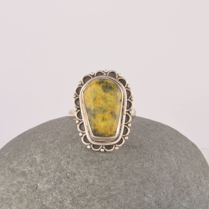 May include: A silver ring with a yellow and green gemstone set in a decorative, scalloped bezel.