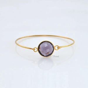 May include: A gold bangle bracelet with a single round purple gemstone.
