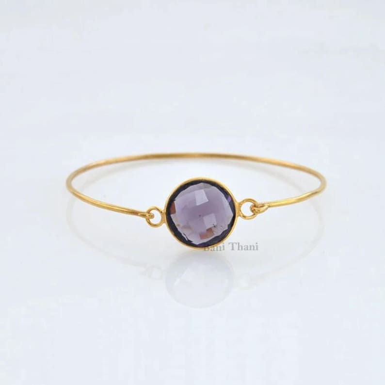 May include: A gold bangle bracelet with a single round purple gemstone.