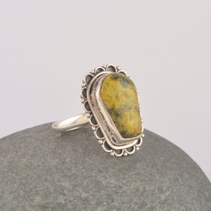 May include: A silver ring with a green and yellow gemstone set in a decorative silver setting.