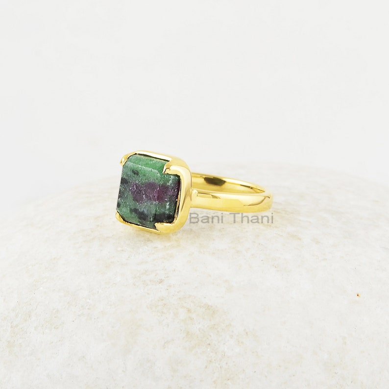 Puede incluir: Anillo de oro con una piedra preciosa cuadrada verde y rosa. El anillo est&aacute; engastado en una banda de oro y tiene un engaste cuadrado. La piedra preciosa es una zoisita verde y rosa.