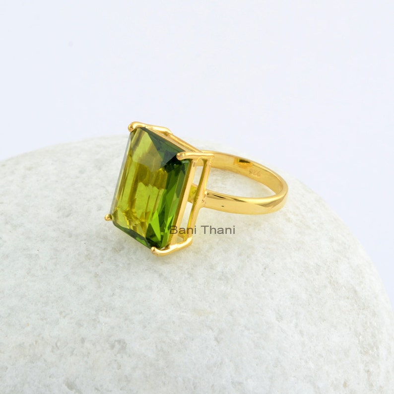 May include: A gold ring with a large, emerald green gemstone. The ring is set in a simple, modern style.