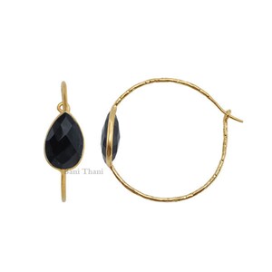 Puede incluir: Aretes de aro de oro con una piedra preciosa negra en forma de lágrima. Los aretes son simples y elegantes.