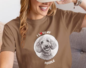 May include: Brown t-shirt featuring a poodle illustration inside a white circle, with the text "I ❤️ my Poodle". The shirt is worn with a beige baseball cap.