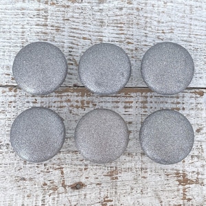 May include: Six silver glitter round cabinet knobs on a white wood background.