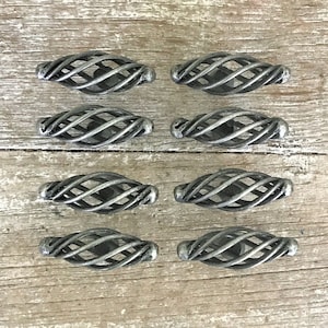 Puede incluir: Ocho pomos de armario de metal plateado con un diseño tejido decorativo. Los pomos están dispuestos en dos filas de cuatro sobre una superficie de madera marrón claro.