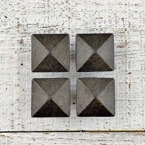 May include: Four black metal pyramid-shaped furniture feet or decorative accents on a white wood background.