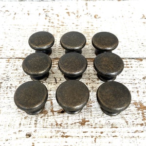 May include: Ten antique bronze cabinet knobs with a round shape and a slightly raised edge. The knobs have a distressed finish, giving them a vintage look.