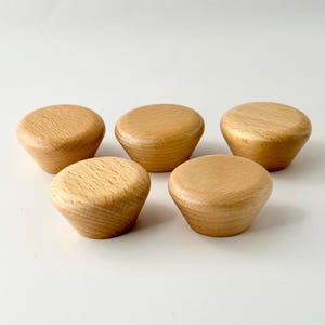 May include: Five wooden knobs in a light brown colour. The knobs are round and have a slightly pointed bottom.