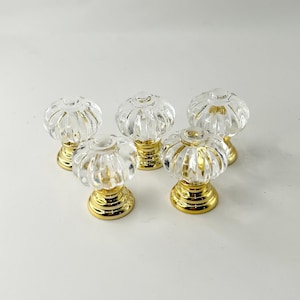 May include: Four clear glass cabinet knobs with gold metal bases. The knobs have a fluted design and are perfect for adding a touch of elegance to any room.