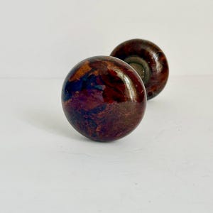 May include: Two antique door knobs with a glossy, mottled finish in shades of brown, burgundy, and hints of blue. The knobs are round with a classic design, perfect for adding vintage charm to any door.