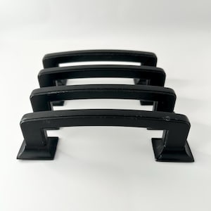 Peut inclure: Trois poignées de meuble en métal noir avec une base carrée et une poignée incurvée.
