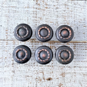 May include: Six round, black cabinet knobs with a copper-coloured ring around the edge. The knobs have a raised, circular design in the centre.