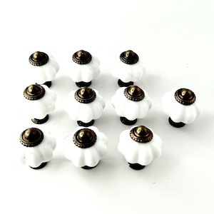 May include: Ten white ceramic cabinet knobs with a brass finish. Each knob has a raised, rounded top and a scalloped edge.