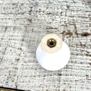 Peut inclure: Bouton de porte en c&eacute;ramique blanche avec une vis en laiton. Le bouton est rond et a une surface lisse.