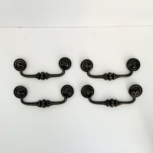 May include: Four antique bronze drawer pulls with a curved handle design. Each pull features a decorative backplate and a central, ornate detail. The pulls are arranged in two rows of two against a white background.