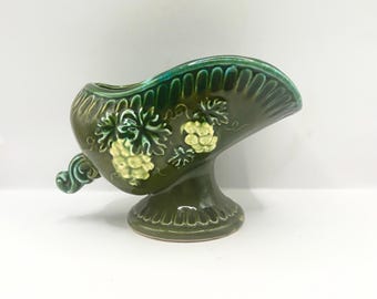 May include: A dark green ceramic serving dish with a pedestal base. The dish features embossed grape and leaf designs in a lighter green color. The rim is a darker shade of green.