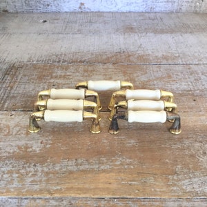 Könnte beinhalten: Satz von sechs Vintage-Schrankknöpfen mit einem weißen Keramikgriff und einer goldenen Metallbasis.
