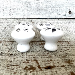 Peut inclure: Quatre boutons de tiroir en c&eacute;ramique blanche avec un motif floral noir et gris. Les boutons ont un dessus arrondi et une tige.