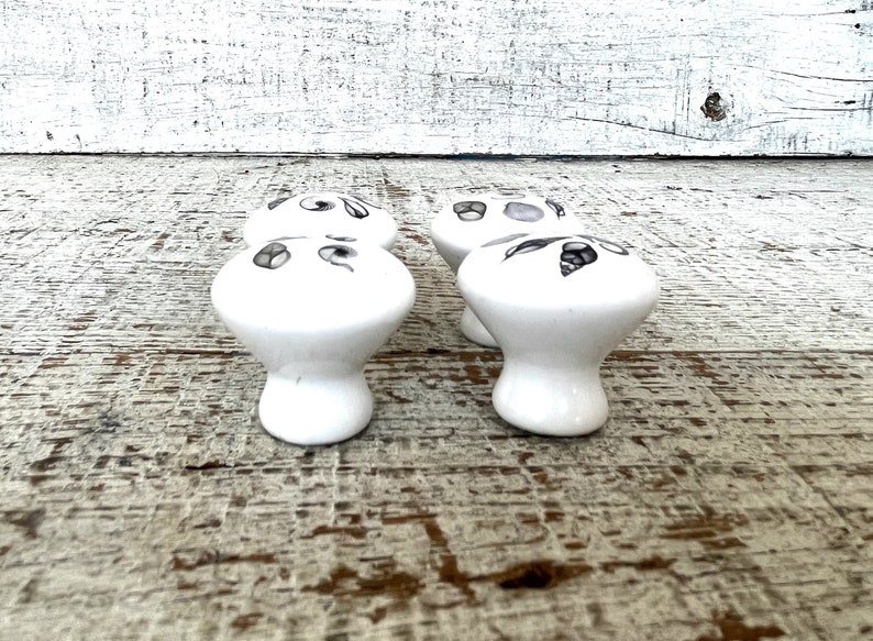 Peut inclure: Quatre boutons de tiroir en c&eacute;ramique blanche avec un motif floral noir et gris. Les boutons ont un dessus arrondi et une tige.