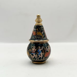 May include: A black and gold decorative jar with a conical lid. The jar features painted figures in colorful clothing, with gold accents. The lid is topped with a gold finial. The jar is likely ceramic or porcelain.