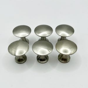 May include: Six silver cabinet knobs with a round, slightly domed top and a short, cylindrical base.