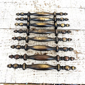 Puede incluir: Conjunto de ocho tiradores de armario de latón antiguo con detalles ornamentados. Cada tirador tiene una manija larga y delgada con un pomo decorativo en cada extremo.
