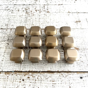 Puede incluir: Doce pomos cuadrados de armario dorados con acabado cepillado.